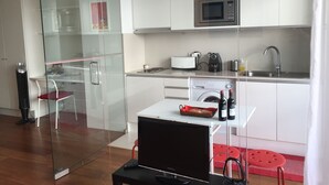 Une cuisine moderne avec des meubles blancs, un four à micro-ondes, un grille-pain et un évier. Une cloison en verre sépare la cuisine d’un coin repas.