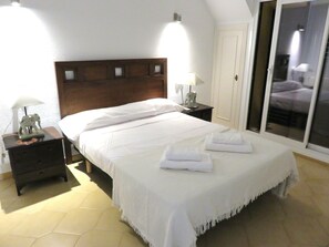 A neatly made bed with white linens, a nightstand with a lamp and a decorative elephant figurine, and a sliding glass door leading to a balcony. - ALBIR house ideally located - 100M from the sea - perfect for 2 to 8 people (Albir)