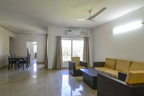 A spacious living room with a sofa, a coffee table, a dining table with chairs, and a ceiling fan. - TripThrill Prudential Pristine Apartment (Colva)