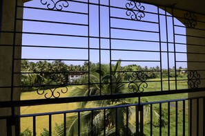 A view through a barred window with a clear sky, palm trees, and a distant building. - TripThrill Prudential Pristine Apartment (Colva)