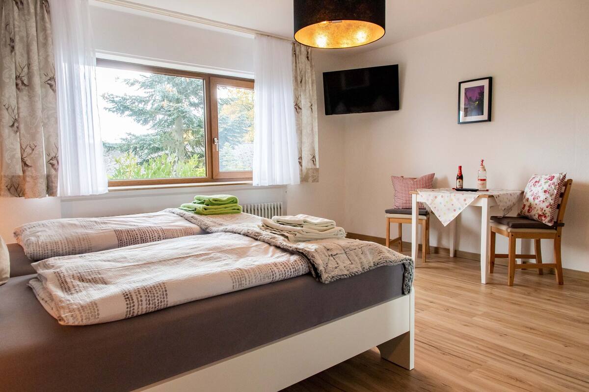 Een slaapkamer met een bed, bureau, stoel, televisie en een raam met gordijnen.