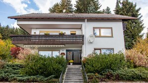 Une maison à deux étages avec un balcon, une antenne parabolique et un mur de pierre à l’avant.