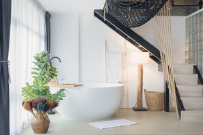Un baño moderno con una bañera grande, un tocador de madera, una planta en maceta y una escalera con barandilla de cuerda.