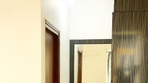 A hallway with a wooden door, a mirror reflecting a bedroom with a bed and a window, and a dark wooden wardrobe. - TripThrill Maytas Hill Apartments (Hyderabad)