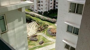A high-rise residential building with multiple balconies, a landscaped garden with pathways, and a view of other buildings in the background. - TripThrill Maytas Hill Apartments (Hyderabad)