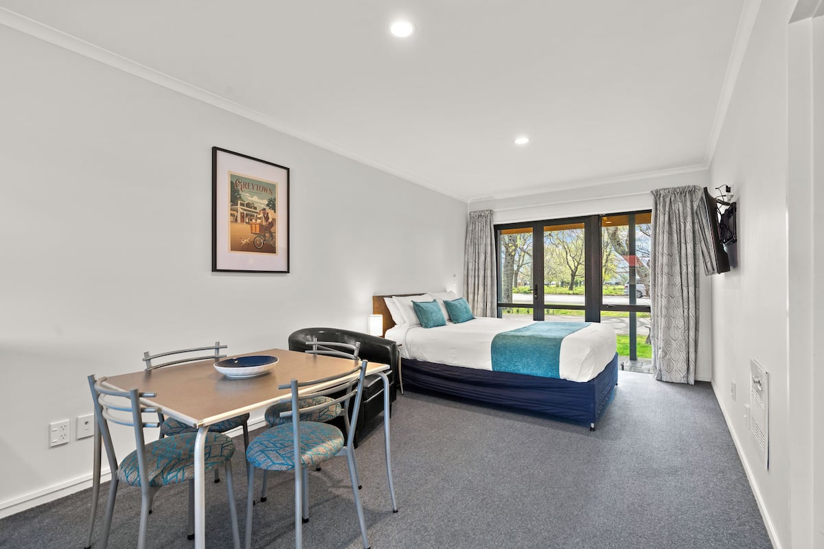 A hotel room with a bed, a dining table with chairs, a framed picture on the wall, and a window with curtains.