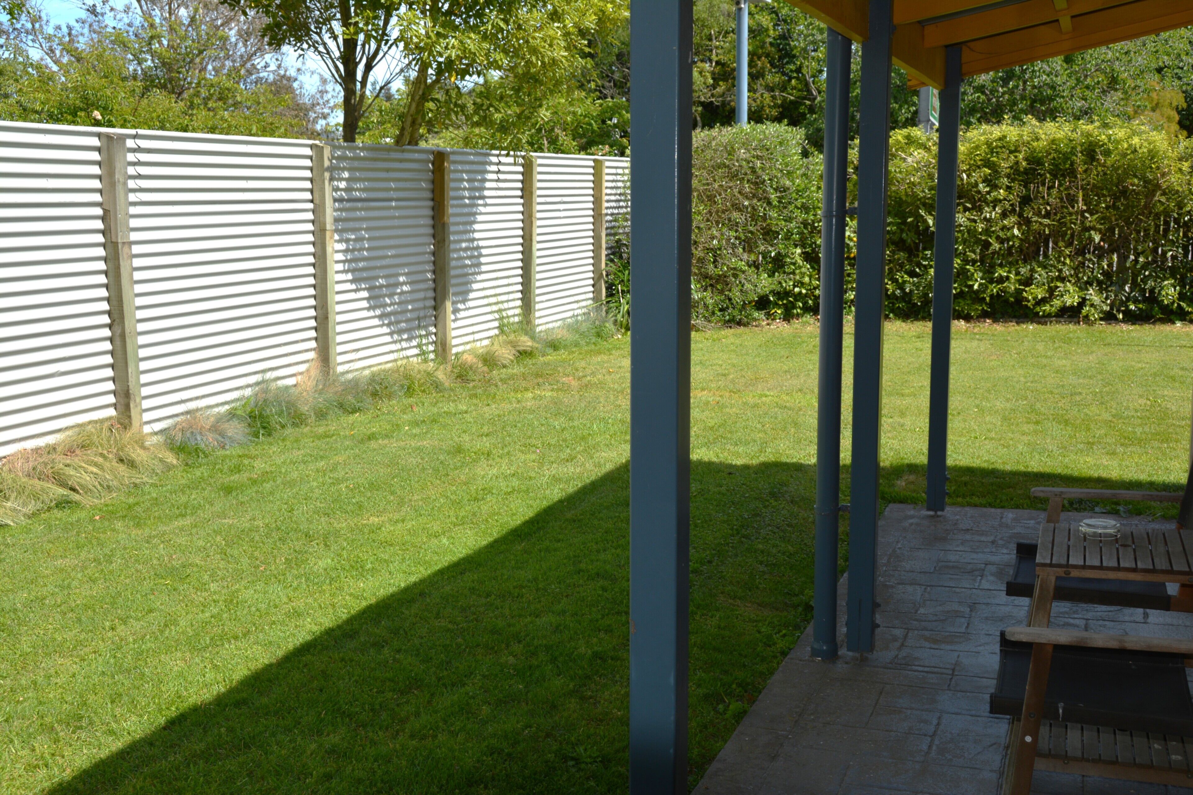 A covered patio area with a wooden bench and a picnic table, surrounded by a well-maintained lawn and a metal fence.