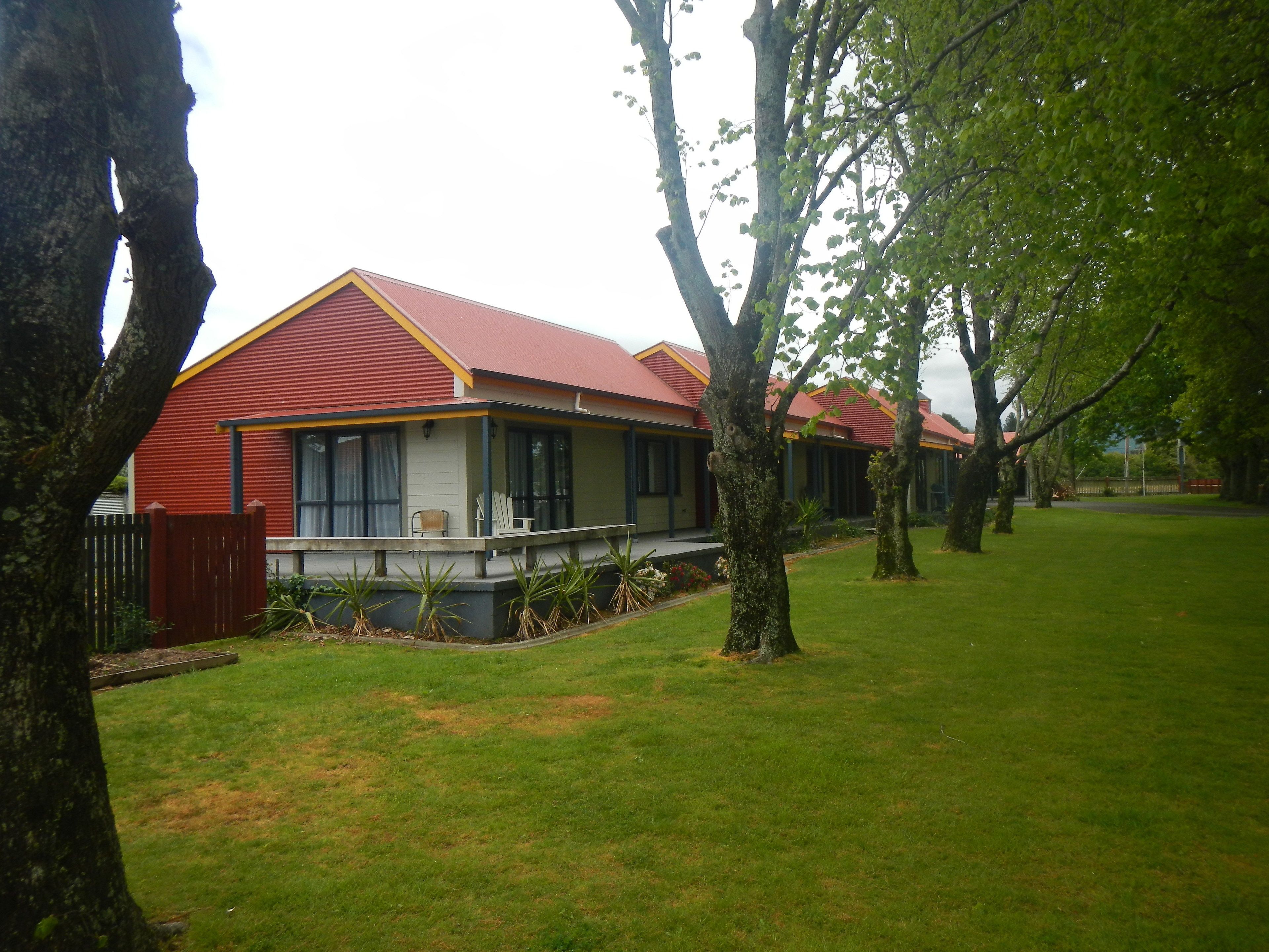 A row of single-story houses with red roofs and white walls, surrounded by a grassy lawn and trees.