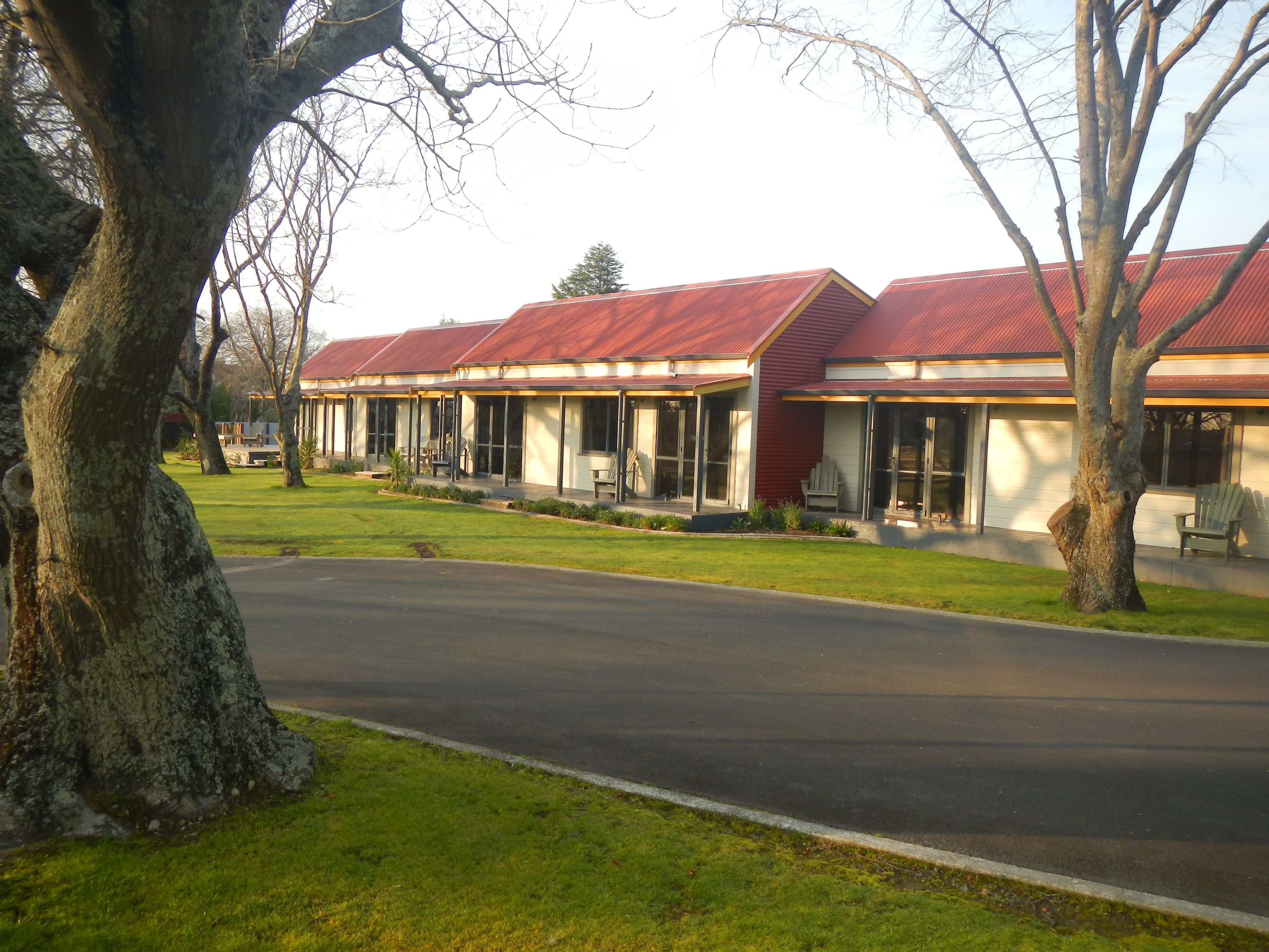 A row of single-story buildings with a red roof, large windows, and a grassy front yard.
