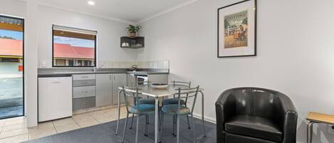 Una cocina moderna con zona de comedor, que incluye una mesa con sillas, un sillón de cuero negro y un cuadro enmarcado en la pared.