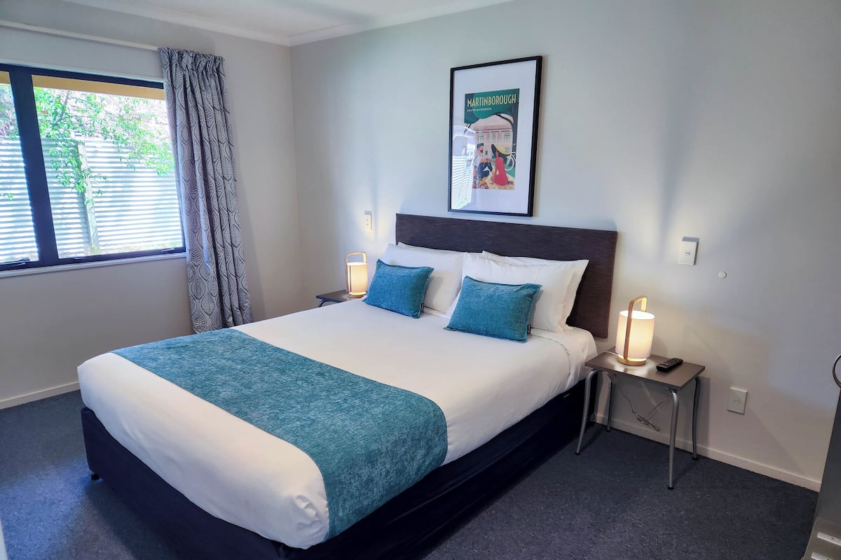 A neatly made bed with a teal throw, two bedside lamps, and a framed picture on the wall.