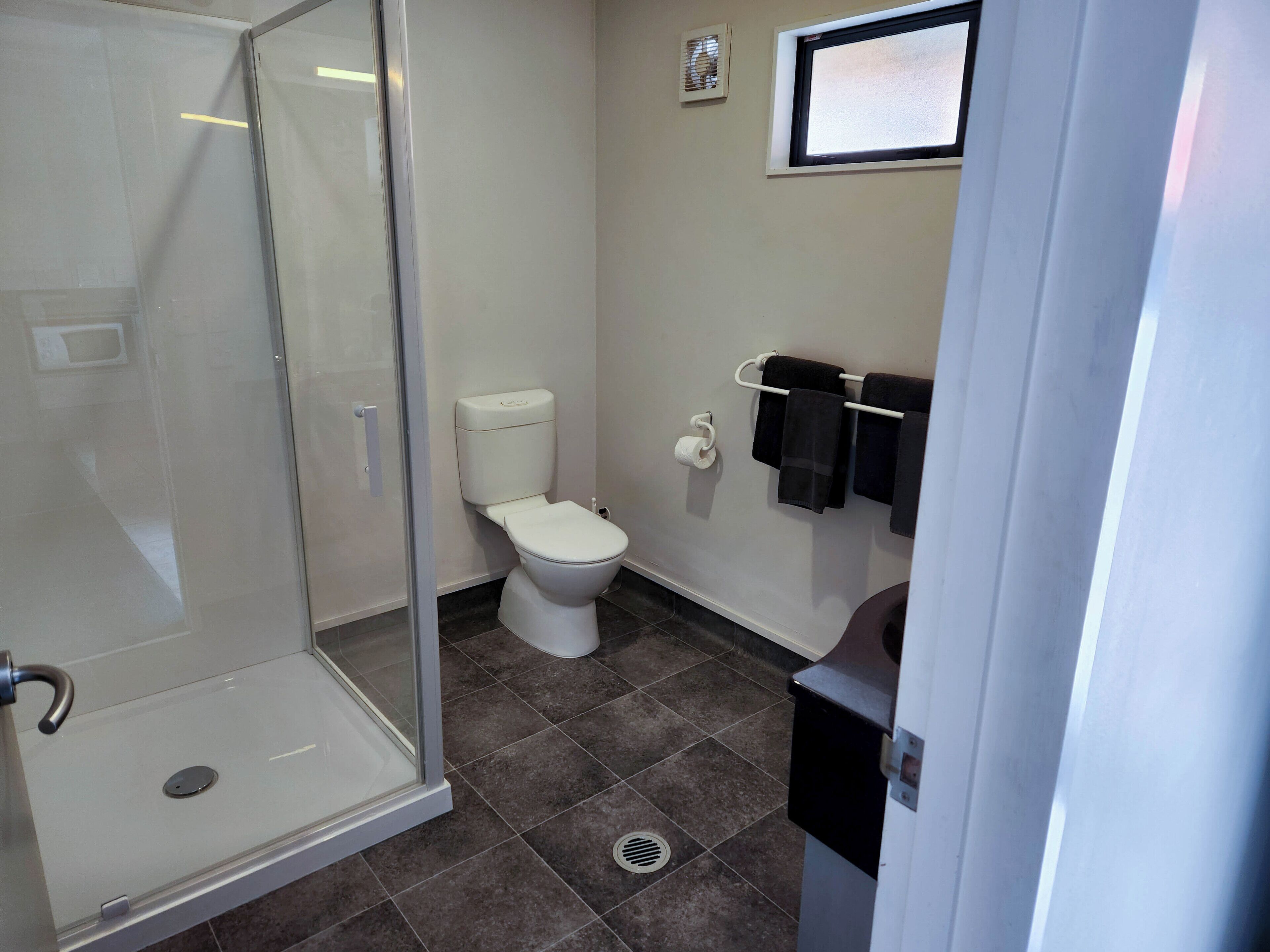 A bathroom with a glass shower enclosure, a toilet, a towel rack with towels, and a vent on the wall.