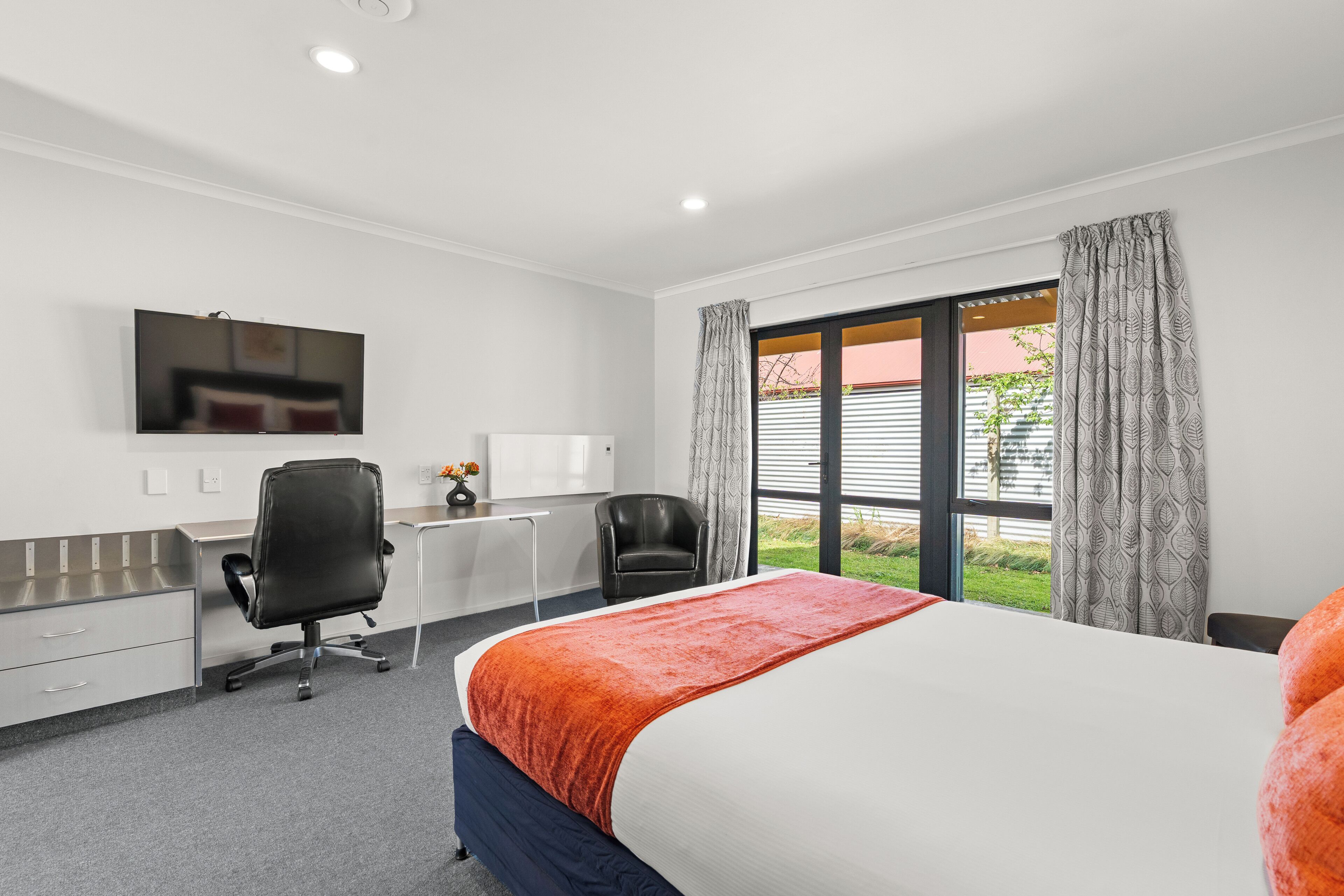 A hotel room with a bed, desk, chair, and a large window with curtains.
