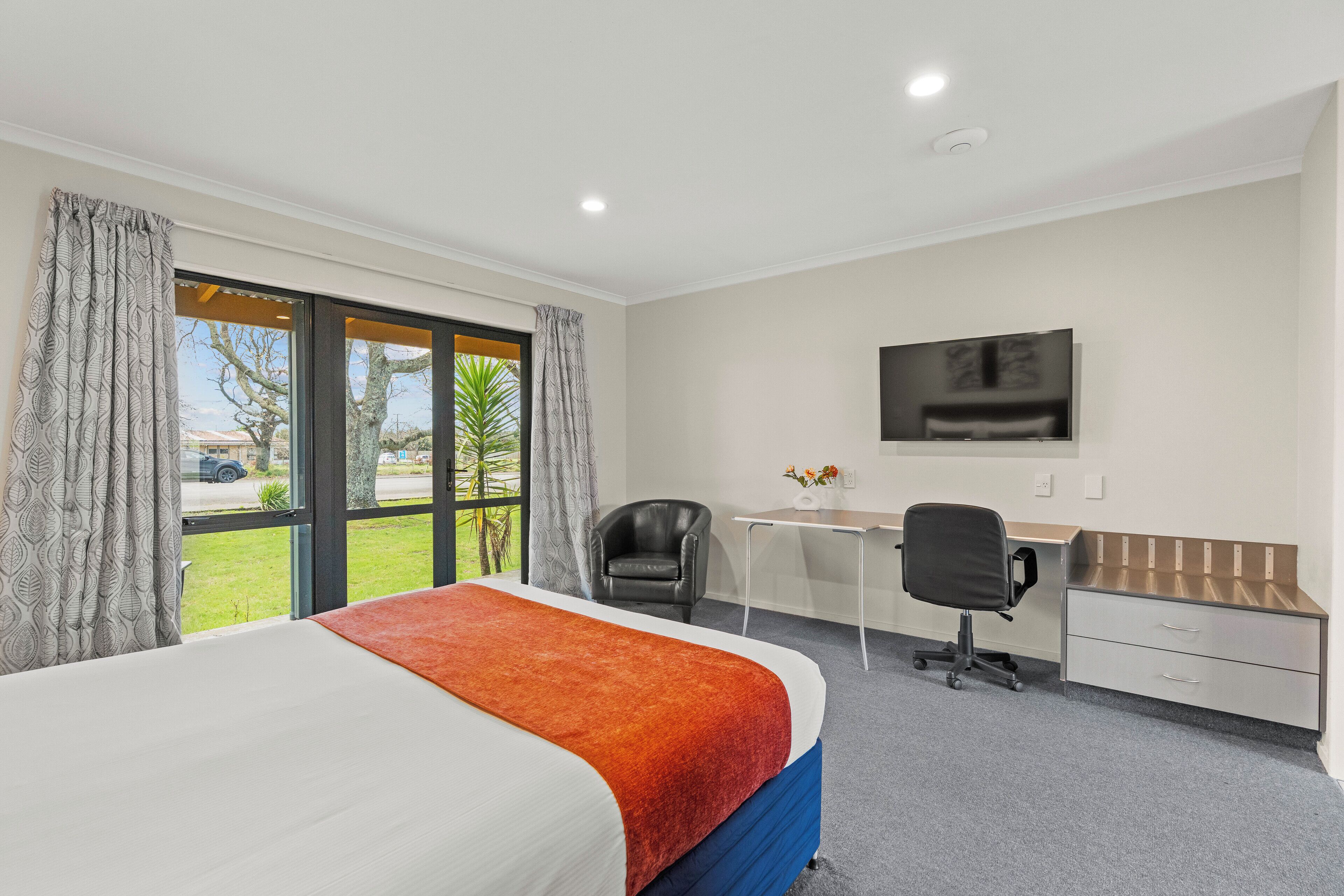 A hotel room with a bed, desk, chair, and a TV on the wall.