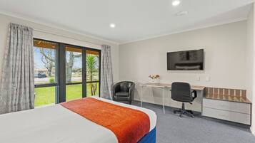 A hotel room with a bed, desk, chair, and a TV on the wall.
