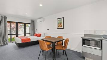 Una habitación moderna con cama, una mesa de comedor con sillas, una kitchenette y un amplio ventanal con cortinas.