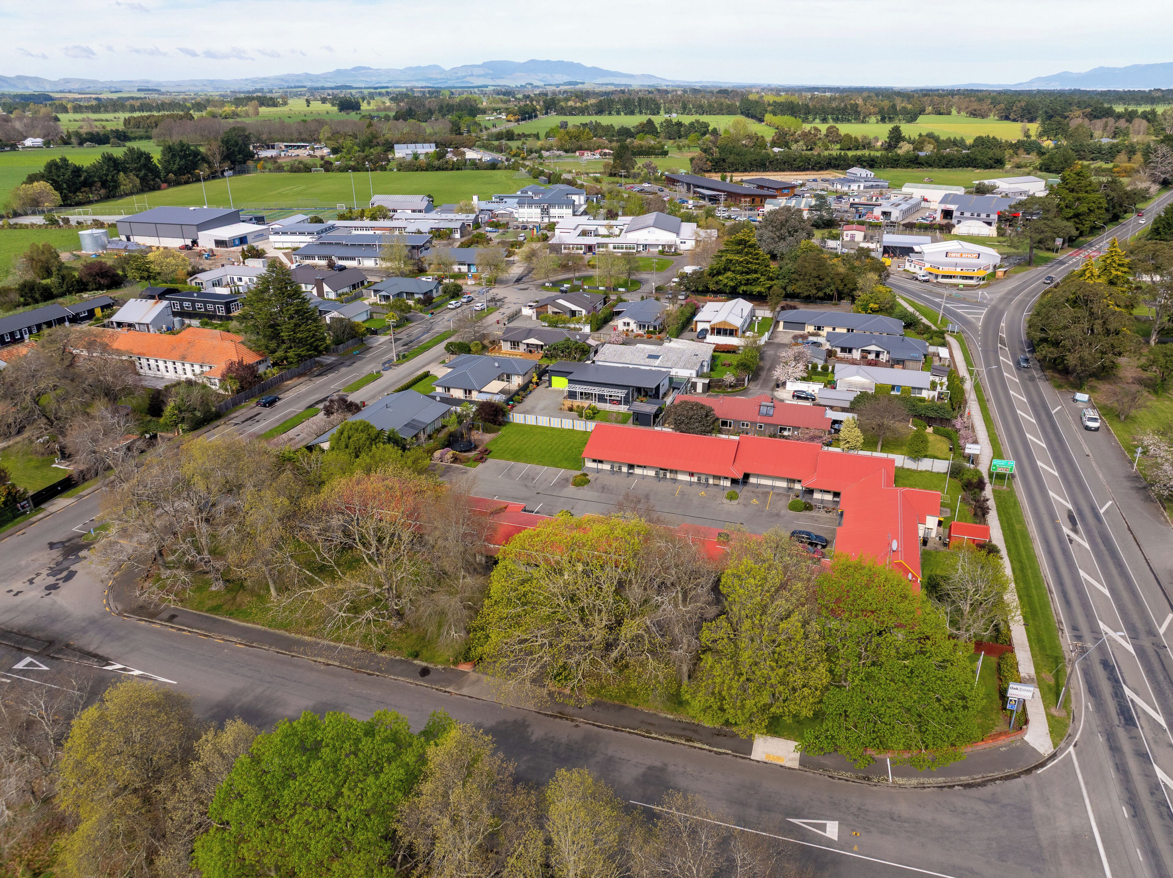 An aerial view of a residential area with houses, a road, and a large building with a red roof.