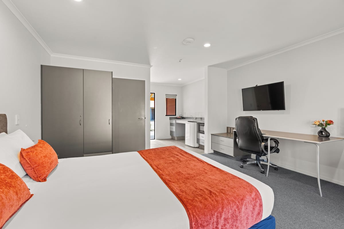 A hotel room with a large bed, a desk, a chair, and a TV mounted on the wall.