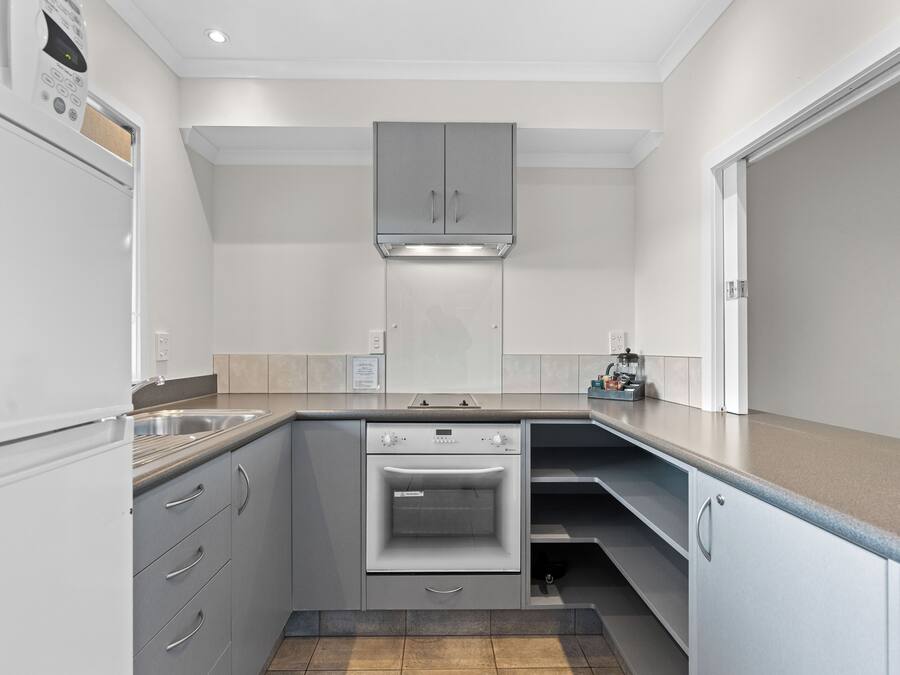 Una cocina compacta con muebles grises, horno empotrado y pileta de acero inoxidable.