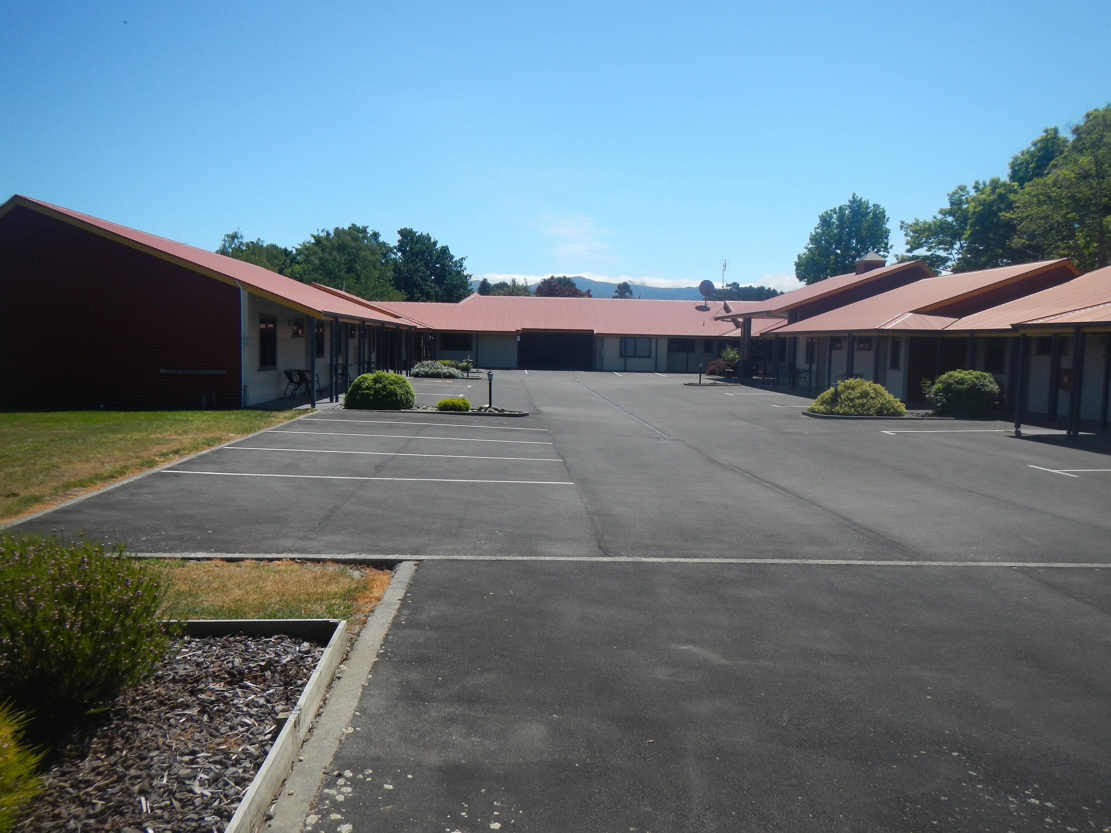 A motel with a central parking lot, multiple rooms with red roofs, and a clear sky.