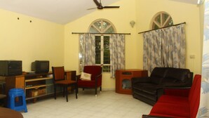 Una sala de estar con televisor, un sofá rojo, un sofá negro, una silla roja y un taburete azul.