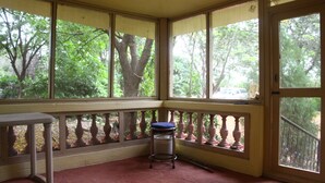 Habitación con alfombra roja, una mesita, un taburete y ventanas amplias que dan a vistas de árboles.