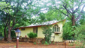 Una casa amarilla con techo rojo, rodeada de árboles y un jardín.