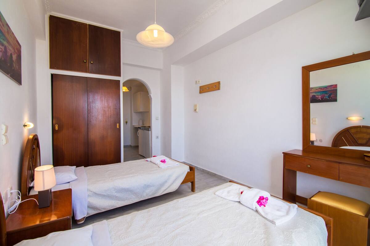A hotel room with two single beds, a wooden wardrobe, a desk with a lamp, and a mirror.