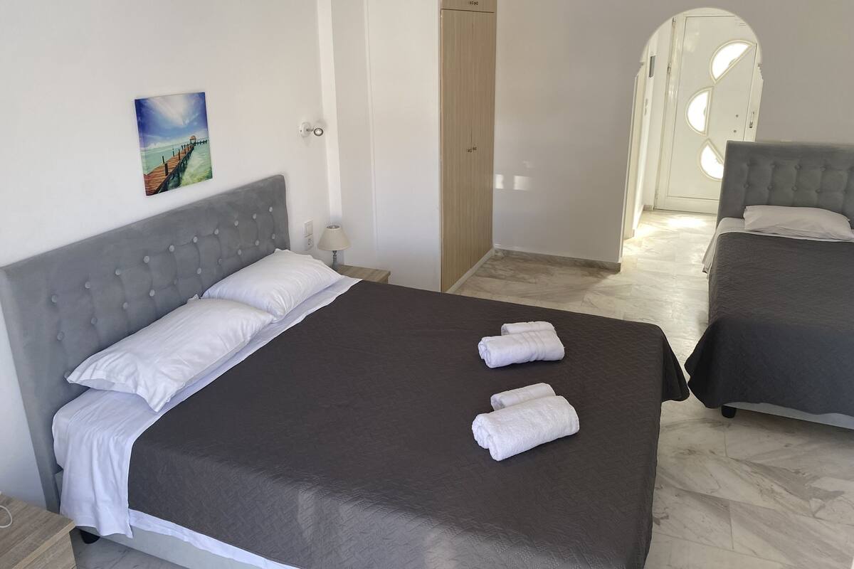 A hotel room with a large bed, two pillows, a bedside lamp, a painting on the wall, and a view of another room.