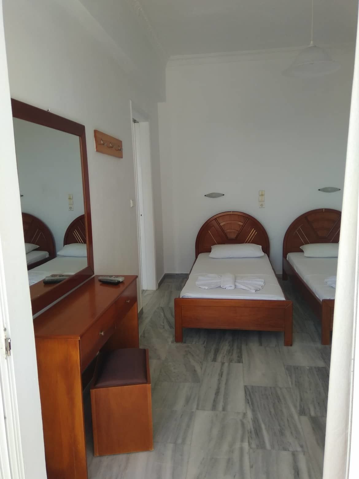 A hotel room with two single beds, a wooden dresser, a mirror, and a small wooden bench.