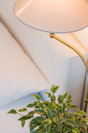 Um abajur com cúpula transparente e base dourada, posicionado ao lado de uma planta com folhas variegadas.