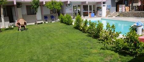 A hotel with a swimming pool, a grassy lawn, and a few trees.