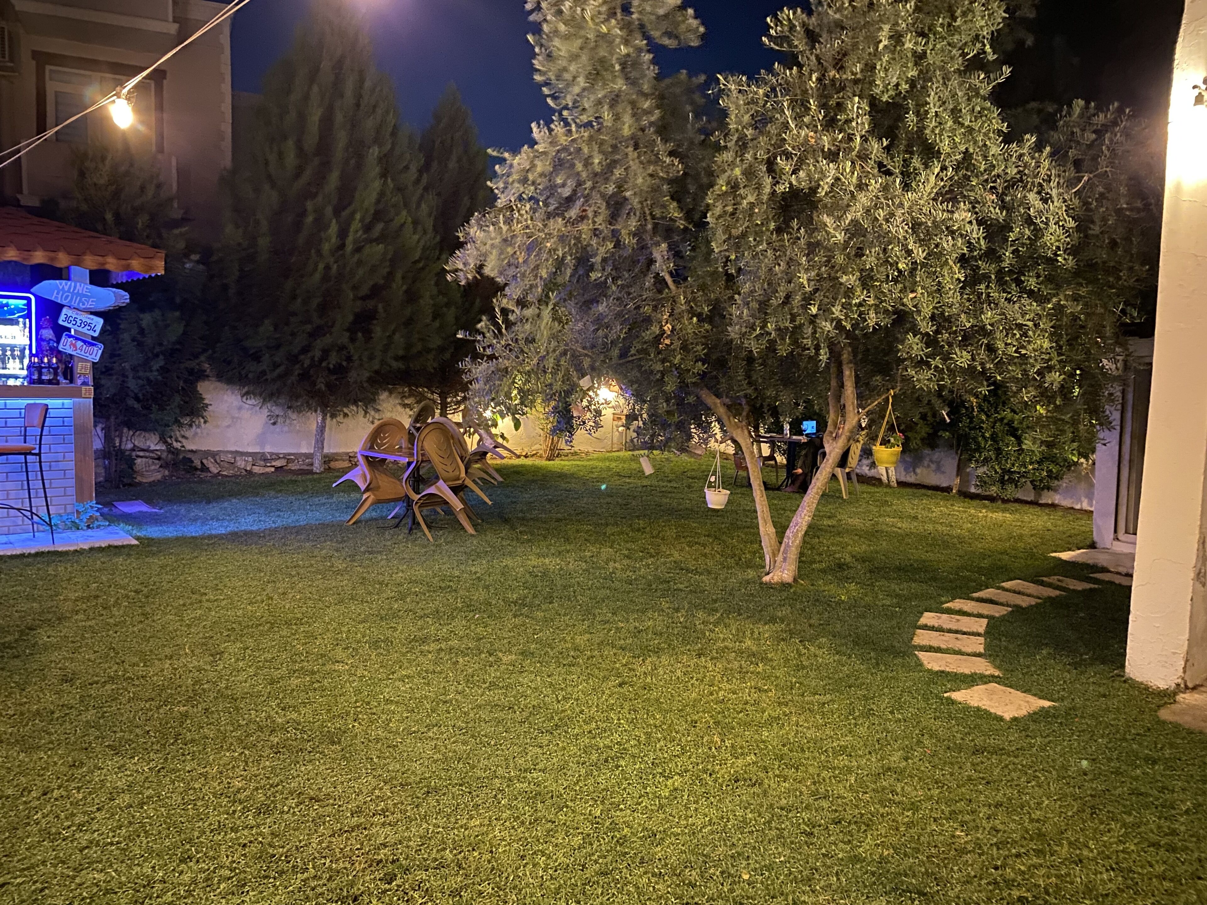Un espacio exterior bien iluminado con césped, una zona de estar con sillas y un bar con un letrero que indica una vinoteca.