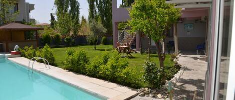 A swimming pool with a tiled deck, surrounded by a well-maintained lawn and various plants.