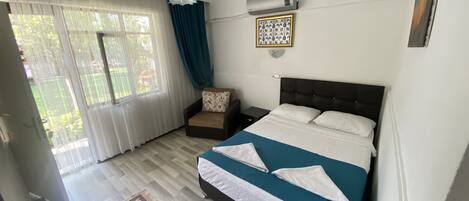 A bedroom with a bed, a chair, a nightstand, a heater, and a window with curtains.