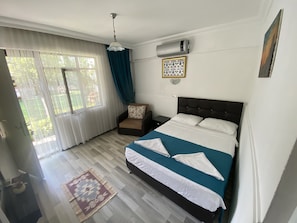 A bedroom with a bed, a chair, a nightstand, a heater, and a window with curtains.