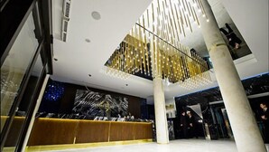 A modern lobby with a reception desk, a high ceiling with a unique light fixture, and marble flooring. - Golden Palace Batumi Hotel & Casino (Batumi)
