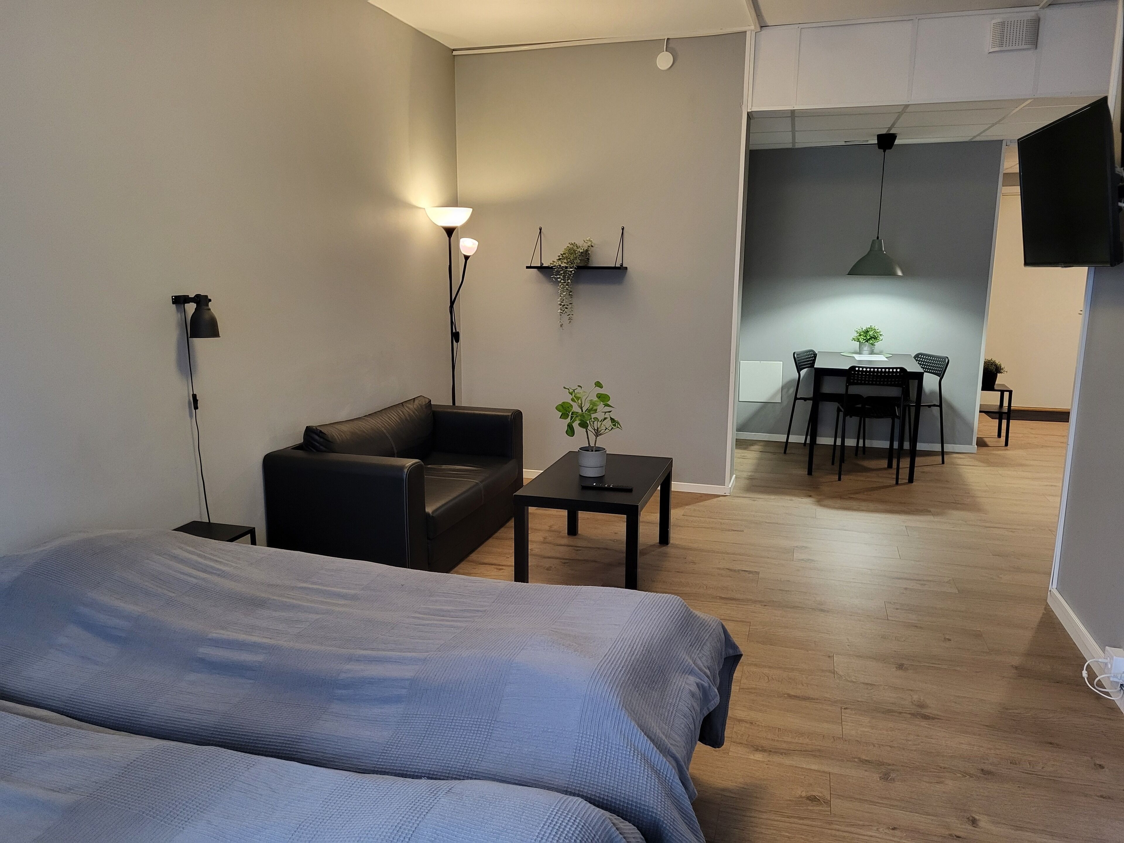 Ein modernes Zimmer mit einem Bett, einem schwarzen Ledersofa, einem kleinen Tisch mit Pflanze und einem Essbereich im Hintergrund.