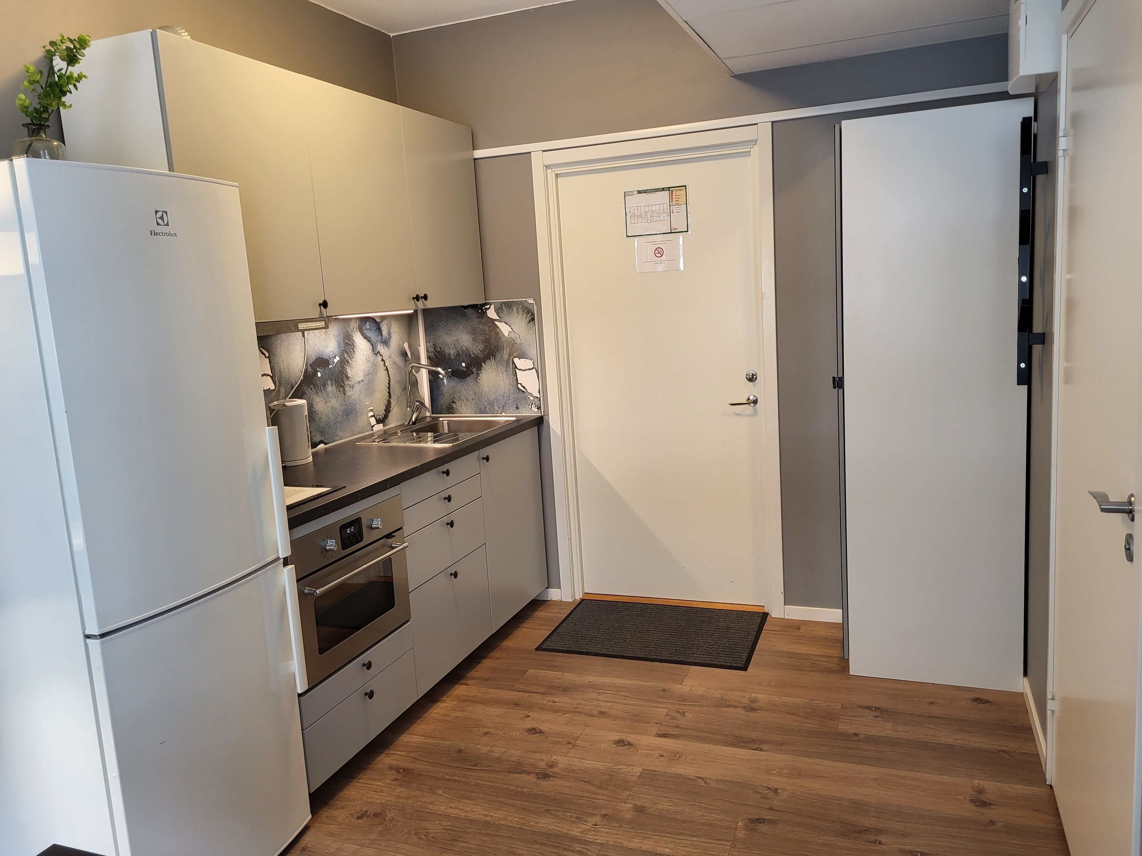 Cocina pequeña con refrigerador, horno, pileta y una puerta con un aviso.