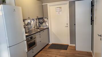 Cocina pequeña con refrigerador, horno, pileta y una puerta con un aviso.