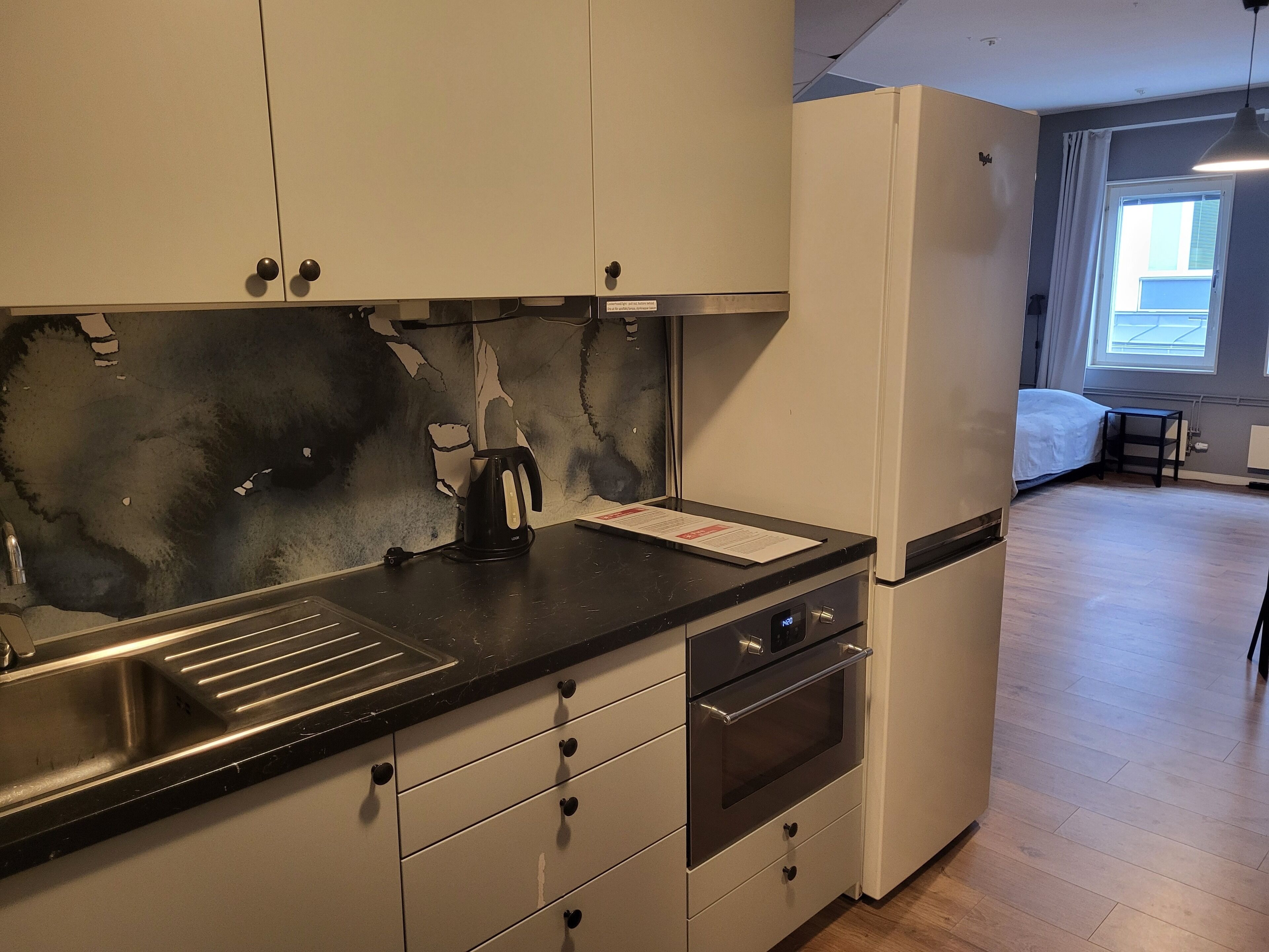 A compact kitchen with a sink, stove, and a kettle on the counter.
