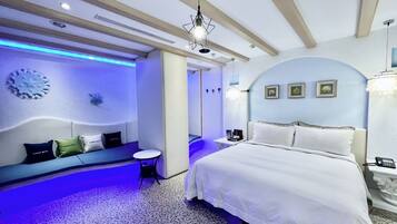 A modern hotel room with a large bed, a seating area with a sofa and chairs, a small table, and a wall-mounted clock.