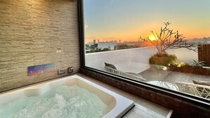 A modern bathroom with a large bathtub, a window with a city view at sunset, and a wooden wall. - Aurora Motel (Taichung)