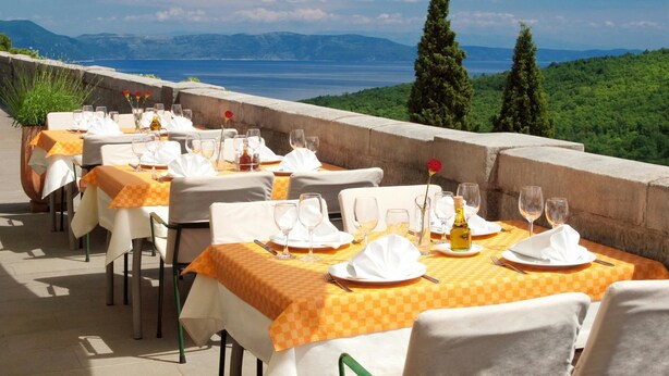 An outdoor dining area with tables set for two, overlooking a scenic landscape with mountains and a body of water. - B&B Kvarner (Labin)