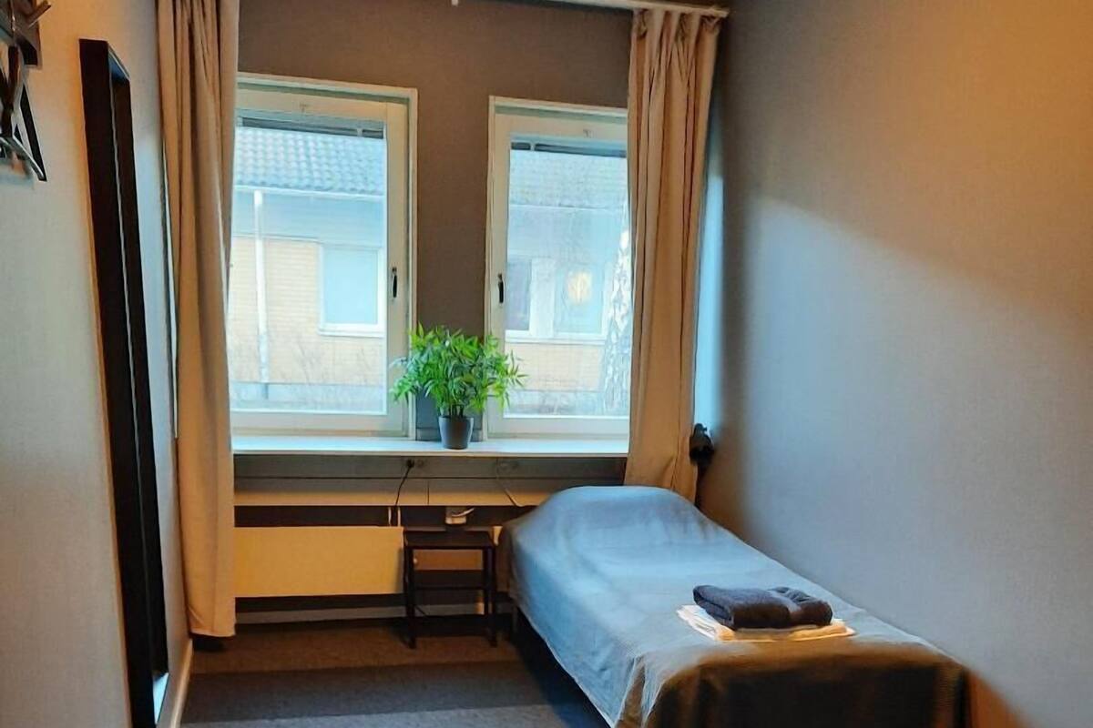 Un dormitorio pequeño y ordenado, con cama, una mesita y una ventana con cortinas.