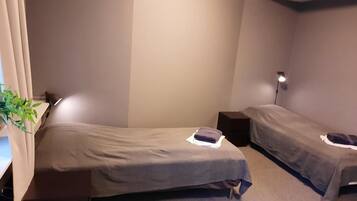 A small, compact room with two single beds, a bedside table, a lamp, and a potted plant.