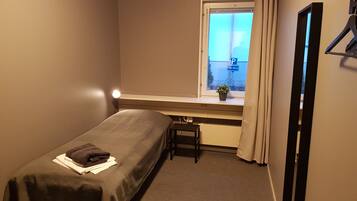 A small, single-bed room with a window, a desk, and a chair.