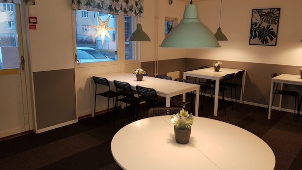 A dining area with tables and chairs, a large star-shaped light decoration, and a view of the street outside. - Vandrarhem Uppsala Portalgatan - Hostel (Uppsala)