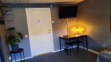 A hotel room with a bed, a desk with a chair, a television mounted on the wall, and a potted plant.