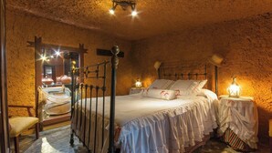 A rustic bedroom with a four-poster bed, a wooden chair, and a small table with a lamp. - GC0004 Cosy cave cottage & private jacuzzi in Fontanales (Moya)